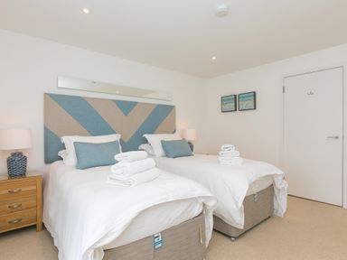 A bedroom with two single beds side by side with white bedding and folded towels on each bed at Portside in Carbis Bay