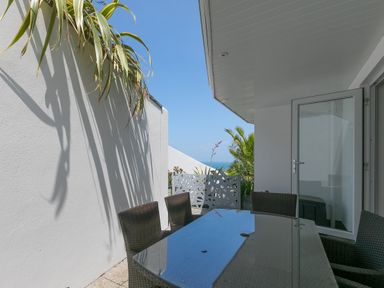 An outdoor patio with a glass table and woven chairs near white walls and an open glass door at Portside in Carbis Bay