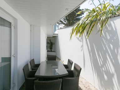 An outdoor dining area with a glass table and six wicker chairs next to white walls and plants at Portside in Carbis Bay