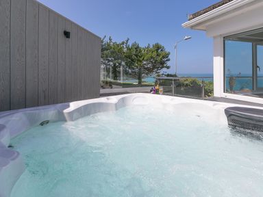 An outdoor hot tub with bubbling water next to a glass railing overlooking trees and the ocean at Portside in Carbis Bay