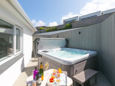 An outdoor patio with a hot tub a small table with drinks and snacks and wooden fencing at Portside in Carbis Bay