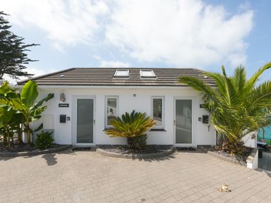 A white building with two frosted glass doors and windows with plants along the front at Portside in Carbis Bay