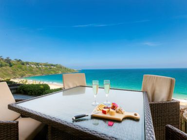 An outdoor table with cheese platter and two glasses overlooking a beach and ocean at Sapphire in Carbis Bay