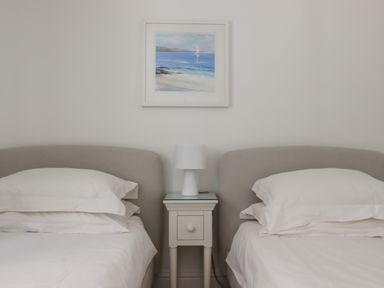 A bedroom with two single beds separated by a nightstand with a lamp and a seascape painting on the wall at Sapphire in Carbis Bay