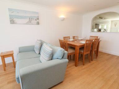 A dining area with a wooden table set for six people next to a light blue sofa in a room at Sapphire in Carbis Bay