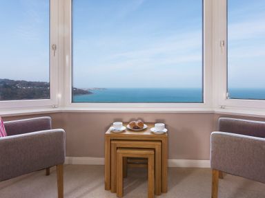 Two chairs and nested tables with cups and a plate of pastries by large windows overlooking the sea at Seathrift in Carbis Bay