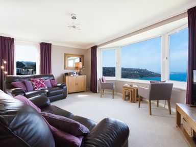A living room with leather sofas armchairs a wooden cabinet and large windows overlooking the sea at Seathrift in Carbis Bay