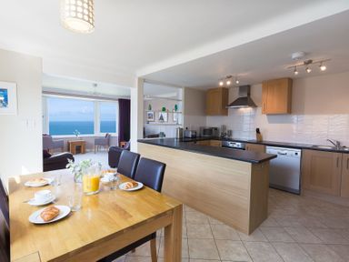 A kitchen with wooden cabinets and a dining table set with croissants and orange juice at Seathrift in Carbis Bay