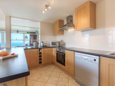 A kitchen with wooden cabinets, a black countertop, stainless steel oven, microwave, and dishwasher at Seathrift in Carbis Bay