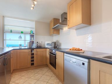 A kitchen with wooden cabinets a dishwasher an oven and croissants on the counter at Seathrift in Carbis Bay