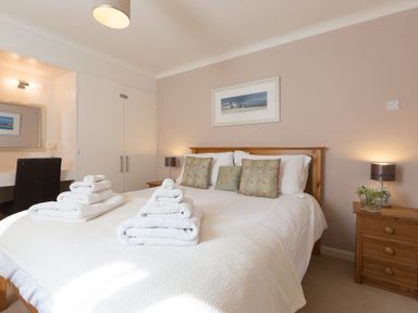 A bedroom with a double bed with folded towels bedside tables with lamps and a dressing table at Seathrift in Carbis Bay