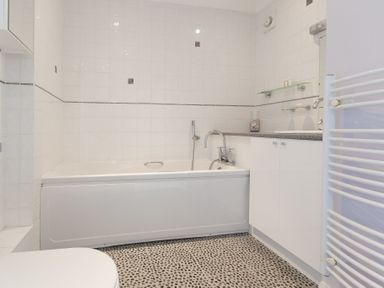 A bathroom with a bathtub a countertop with sink and cabinets and a towel radiator at Seathrift in Carbis Bay