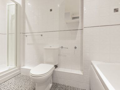 A bathroom with a toilet shower and bathtub with tiled walls and pebble-patterned floor at Seathrift in Carbis Bay