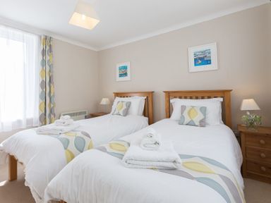 A bedroom with two single beds with white bedding and patterned pillows and curtains at Seathrift in Carbis Bay
