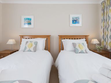 A bedroom with two single wooden beds white bedding bedside tables with lamps and patterned curtains at Seathrift in Carbis Bay