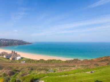 A coastline with a sandy beach and houses near railway tracks at Seathrift in Carbis Bay