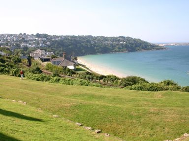 A coastal scene with a beach a grassy hill houses and a person standing near shrubs at Seathrift in Carbis Bay