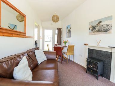 A living room with a brown leather sofa white cushions a small dining table with chairs flowers and pictures on the walls at Chalet 150 Winterton-On-Sea