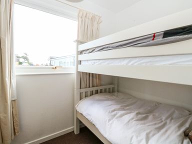 A small bedroom with a white bunk bed next to a window with curtains at Chalet 150 in Winterton-On-Sea