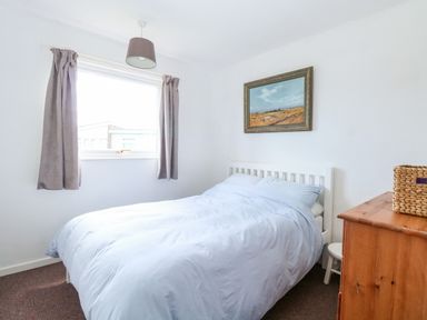 A bedroom with a bed a window with curtains a chest of drawers and a framed painting on the wall at Chalet 150 in Winterton-On-Sea