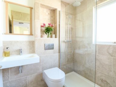 A bathroom with a wall-mounted sink and mirror a toilet and a shower enclosure with a glass partition and window a niche with a vase of pink flowers and a candle at Chalet 150 in Winterton-On-Sea