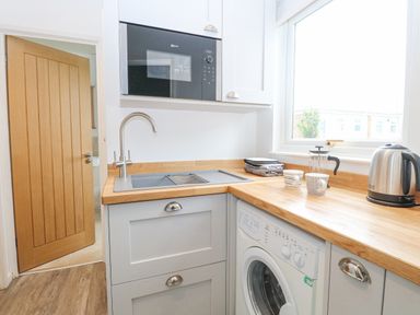 A kitchen with a microwave above a sink and a washing machine under a wooden countertop at Chalet 150 in Winterton-On-Sea