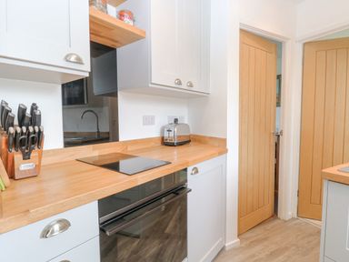 A kitchen with wooden countertops white cabinets a knife set a toaster an induction cooktop and two wooden doors at Chalet 150 in Winterton-On-Sea