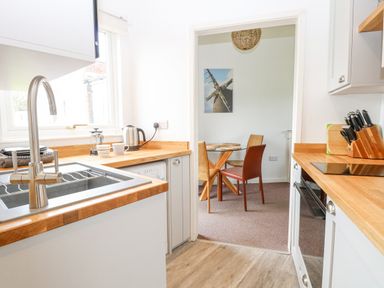 A kitchen with a sink kettle and knives with a dining area with a table and chairs in the background at Chalet 150 in Winterton-On-Sea