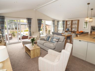 An open living room and dining area with sofas armchairs a wooden coffee table and dining table at Seagull Lodge in Runswick Bay