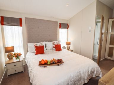 A bedroom with a double bed with red and white cushions bedside tables with lamps and flowers at Seagull Lodge in Runswick Bay