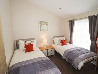 A bedroom with two single beds a nightstand and lamp between them and a window with curtains at Seagull Lodge in Runswick Bay