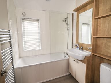 A bathroom with a bathtub shower combination sink with mirror and wooden storage shelves at Seagull Lodge in Runswick Bay