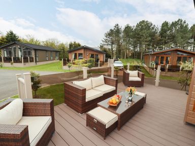An outdoor patio with rattan furniture and a glass table with fruit and wine at Seagull Lodge in Runswick Bay