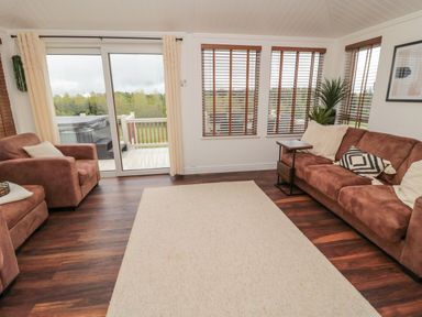 A living room with brown sofas and large windows showing greenery outside at Woodland View Lodge Swarland near Felton