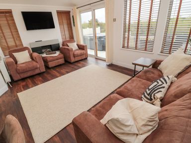 A living room with brown sofas chairs a beige rug and a wall mounted television at Woodland View Lodge Swarland near Felton