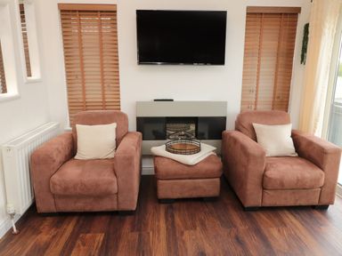 A living room with two armchairs and a footstool with cushions and a tray below a wall-mounted television at Woodland View Lodge Swarland near Felton