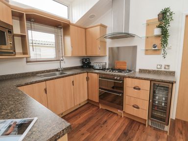 A kitchen with wooden cabinets a gas stove an oven a microwave a sink and a wine cooler at Woodland View Lodge in Swarland near Felton