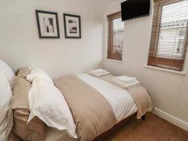 A bedroom with a bed folded towels two framed pictures two windows with blinds and a wall mounted tv at Woodland View Lodge in Swarland near Felton