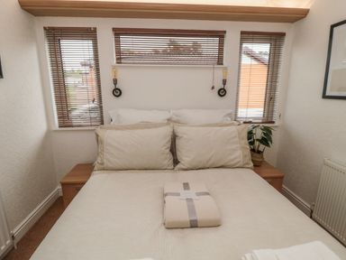 A bedroom with bed pillows folded blanket and windows with blinds at Woodland View Lodge in Swarland near Felton