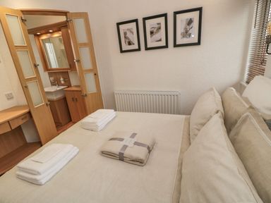 A bedroom with a bed towels and a bathroom with wooden doors at Woodland View Lodge Swarland near Felton