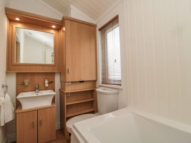 A bathroom with a sink cabinet mirror wooden storage unit toilet window with blinds and bathtub at Woodland View Lodge in Swarland near Felton