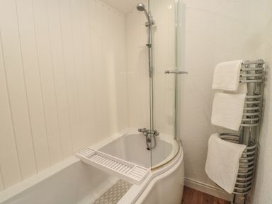 A bathroom with a bathtub, shower head, glass shower screen, towel rack with three white towels at Woodland View Lodge in Swarland near Felton