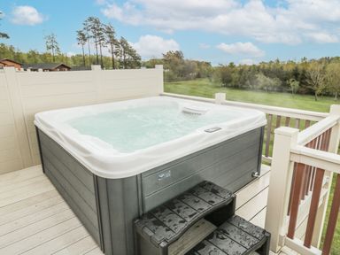 An outdoor hot tub on a wooden deck with plastic stairs and a view of a grassy field and trees at Woodland View Lodge Swarland near Felton