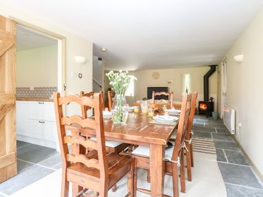 A dining area with a wooden table and chairs set for breakfast a stove and seating area are visible at The Hermitage West Beckham near Sheringham