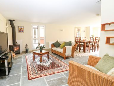 A living room with wood stove tv and wicker sofas and a dining area at The Hermitage in West Beckham near Sheringham