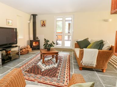 A living room with a wood stove fire a patterned rug a wooden coffee table wicker furniture and a television at The Hermitage in West Beckham near Sheringham