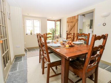 A dining room with a wooden table set for breakfast with chairs and an open door at The Hermitage in West Beckham near Sheringham