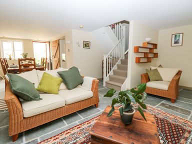 A living room with wicker sofas and green cushions a wooden coffee table with a plant and a dining area in the background at The Hermitage in West Beckham near Sheringham