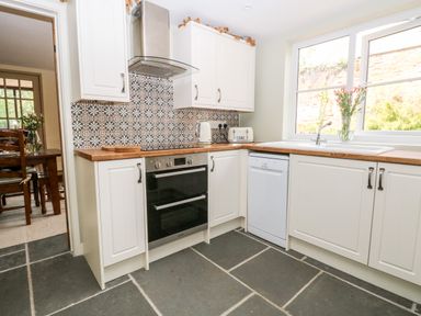 A kitchen with white cabinets a built-in oven a dishwasher and a window with flowers on the sill at The Hermitage West Beckham near Sheringham