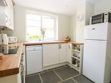 A kitchen with white cabinets wooden countertops a dishwasher a refrigerator a microwave toaster and a window with flowers at The Hermitage in West Beckham near Sheringham